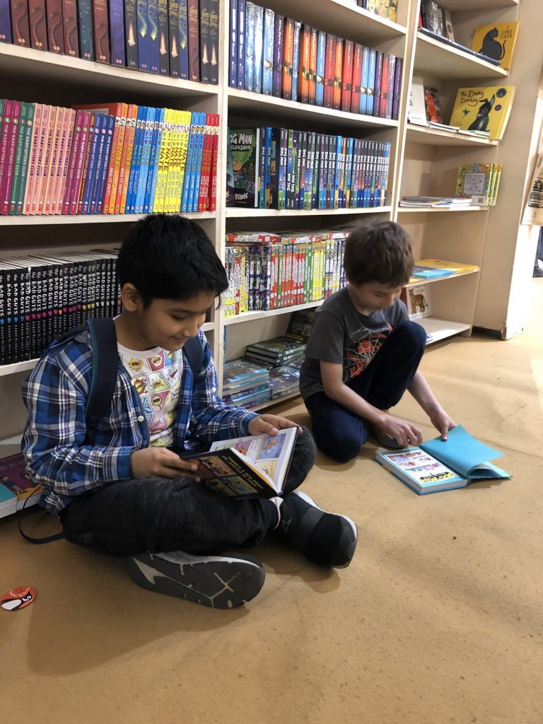 Two boys sitting on the floor reading Dog Man books.