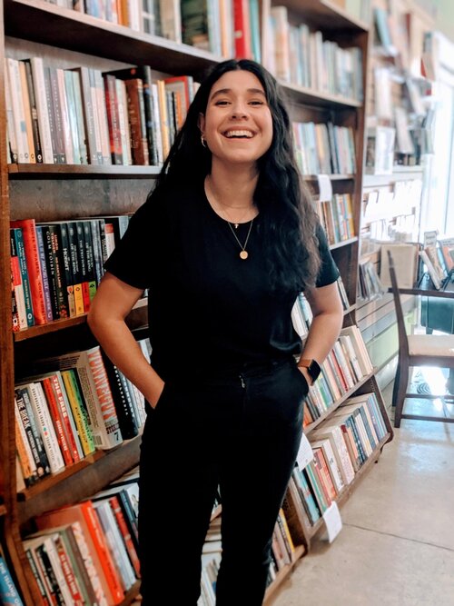 Photo of Leslie Sainz standing in front of a bookshelf